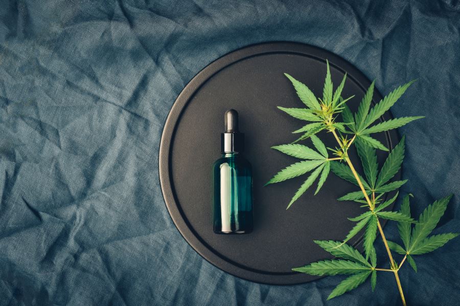 Texte alternatif :Flacon de CBD avec feuille de cannabis sur fond sombre, question sur sa nature de drogue.